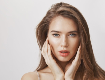 Žena predivnog lica i kože drži ruke na obrazima