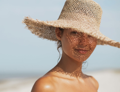 Žena pod širokim slamnatim šeširom stoji na sunčanoj plaži